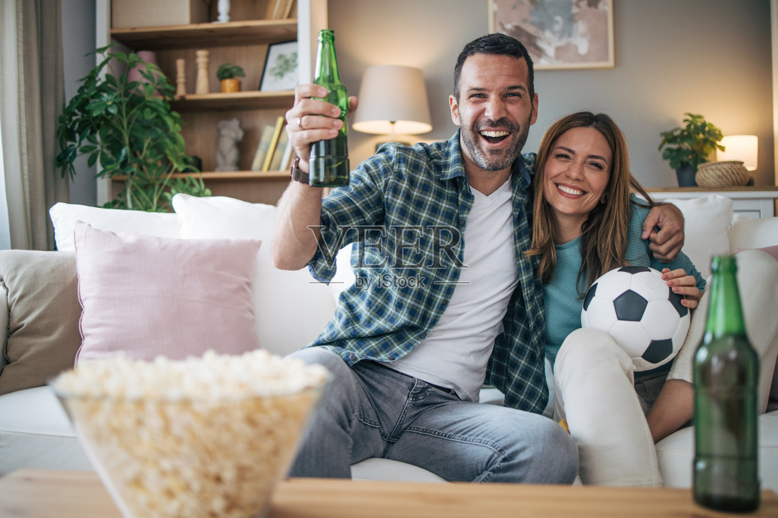 幸福的情侣在家里一起度过周末，坐在沙发上看电视直播的足球比赛，为自己喜欢的球队加油照片摄影图片