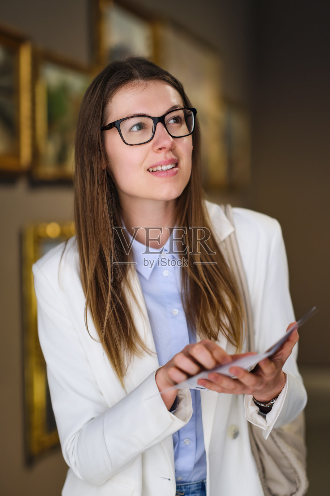 有思想的年轻白人女人戴着眼镜在看展览。博物馆日的概念。照片摄影图片