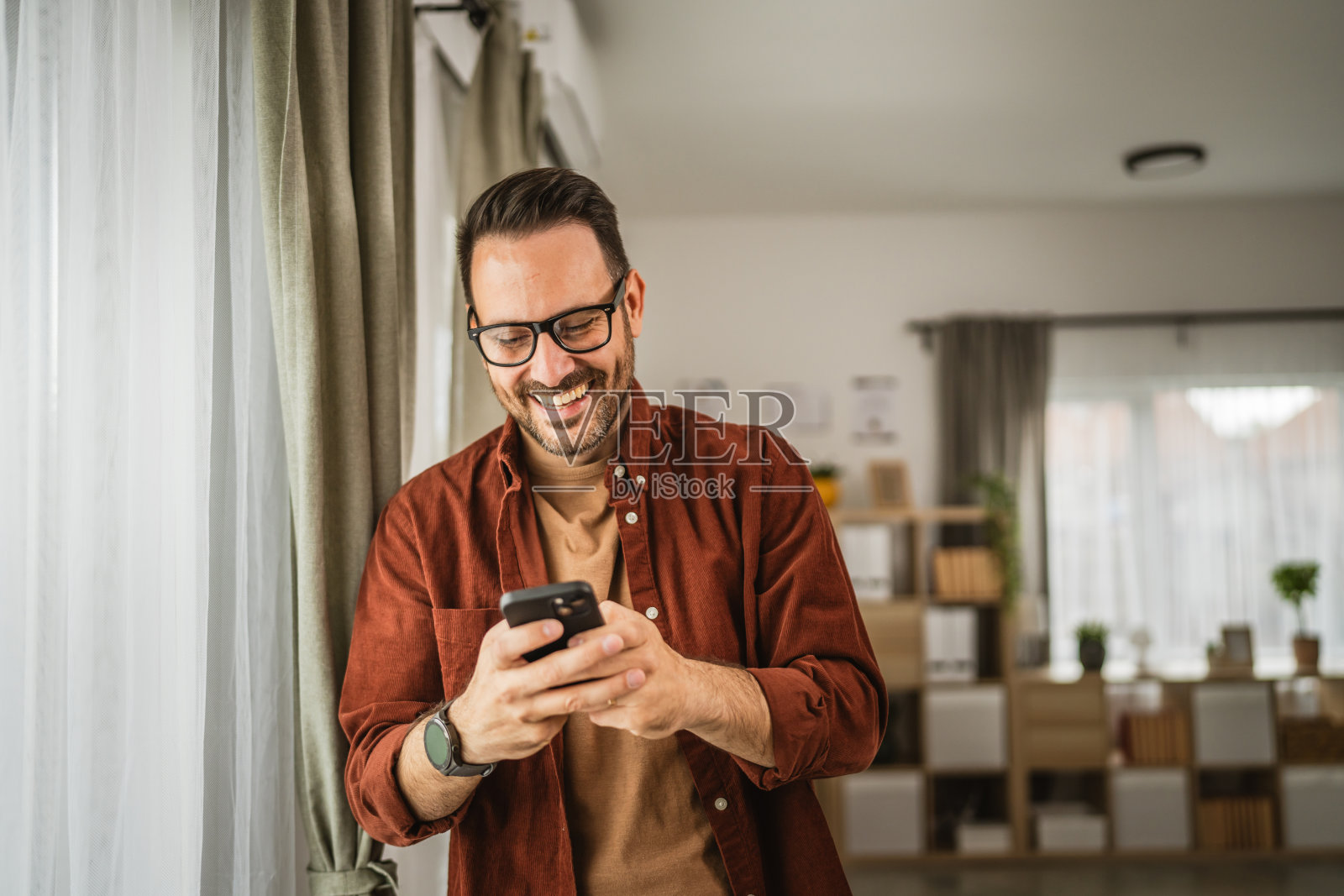 成年男子站在家里拿着手机发短信的画像照片摄影图片