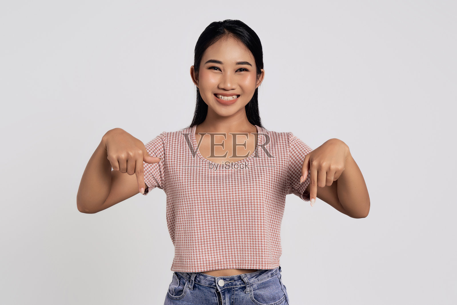 穿着休闲服微笑着快乐的年轻亚洲女子指着白色背景上孤立的复制空间模型。人们的生活方式理念照片摄影图片