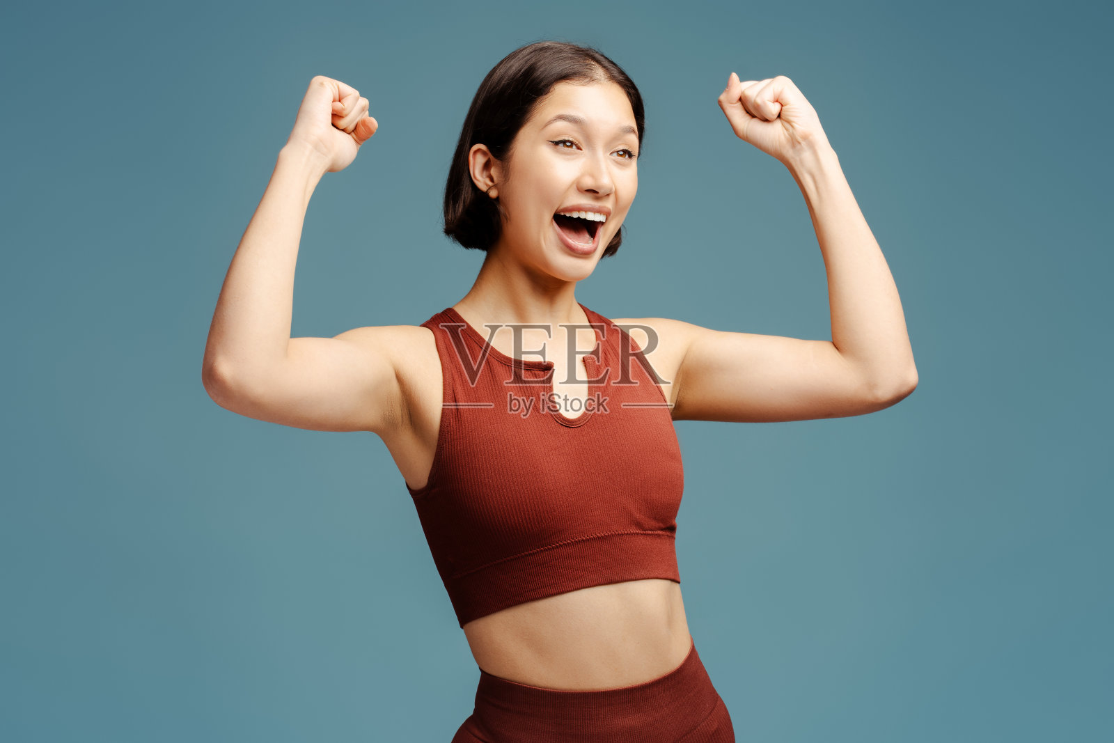 兴奋的黑发女人在蓝色的背景上欢欣鼓舞，望向别处照片摄影图片