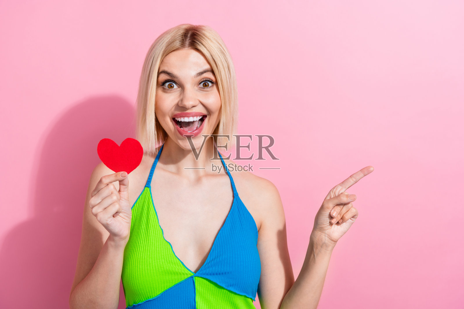 照片欣喜若狂的女孩与鲍勃发型穿着彩色坦克抱心明信片表明空白空间孤立在粉红色的背景照片摄影图片