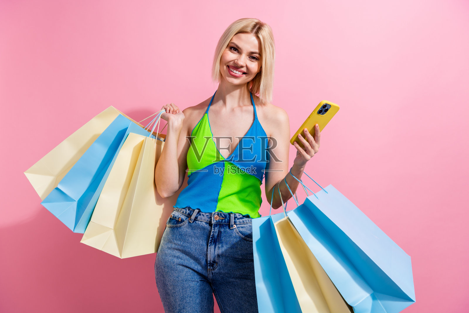 照片的好心情积极的女孩与鲍勃头发穿着彩色坦克持有新衣服的袋子智能手机孤立的粉红色背景照片摄影图片