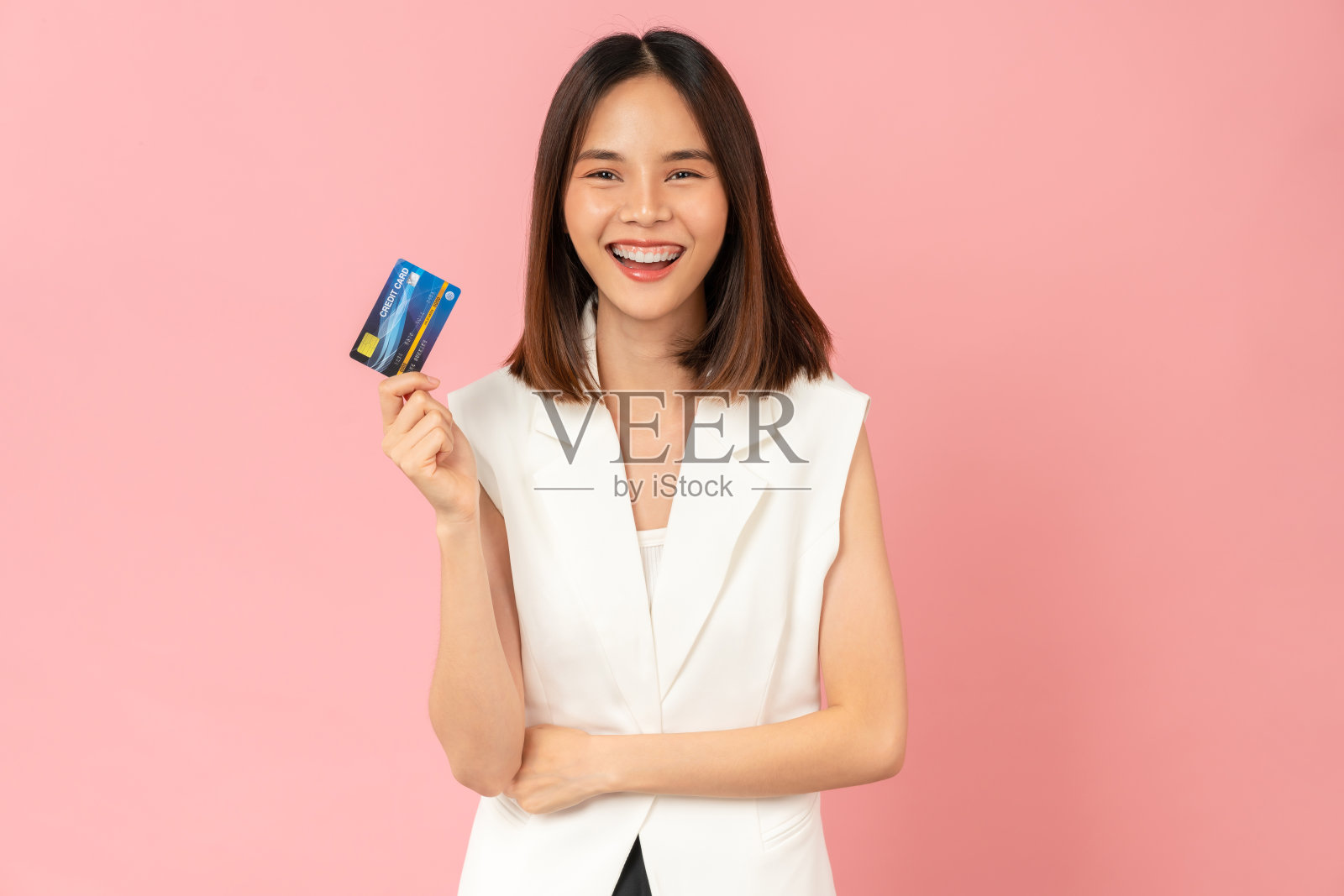 开朗美丽的亚洲女人拿着粉红色背景的信用卡模型。照片摄影图片
