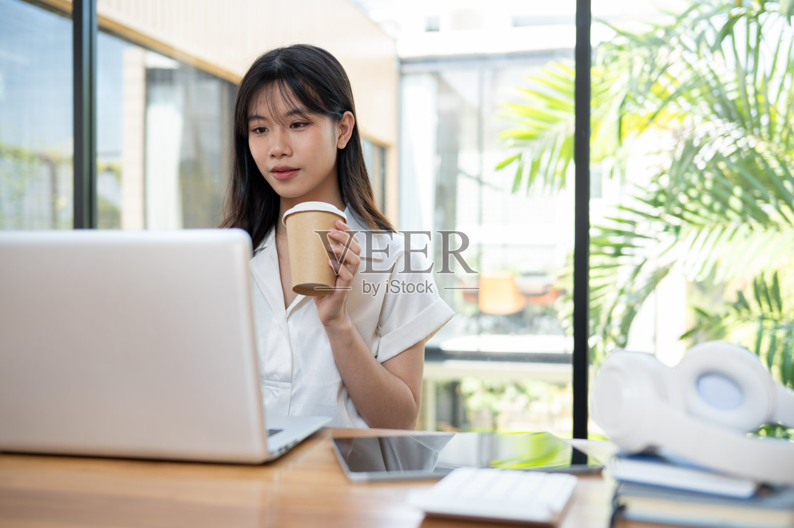 一位美丽的亚洲女商人一边喝着咖啡，一边专注于笔记本电脑上的工作。照片摄影图片