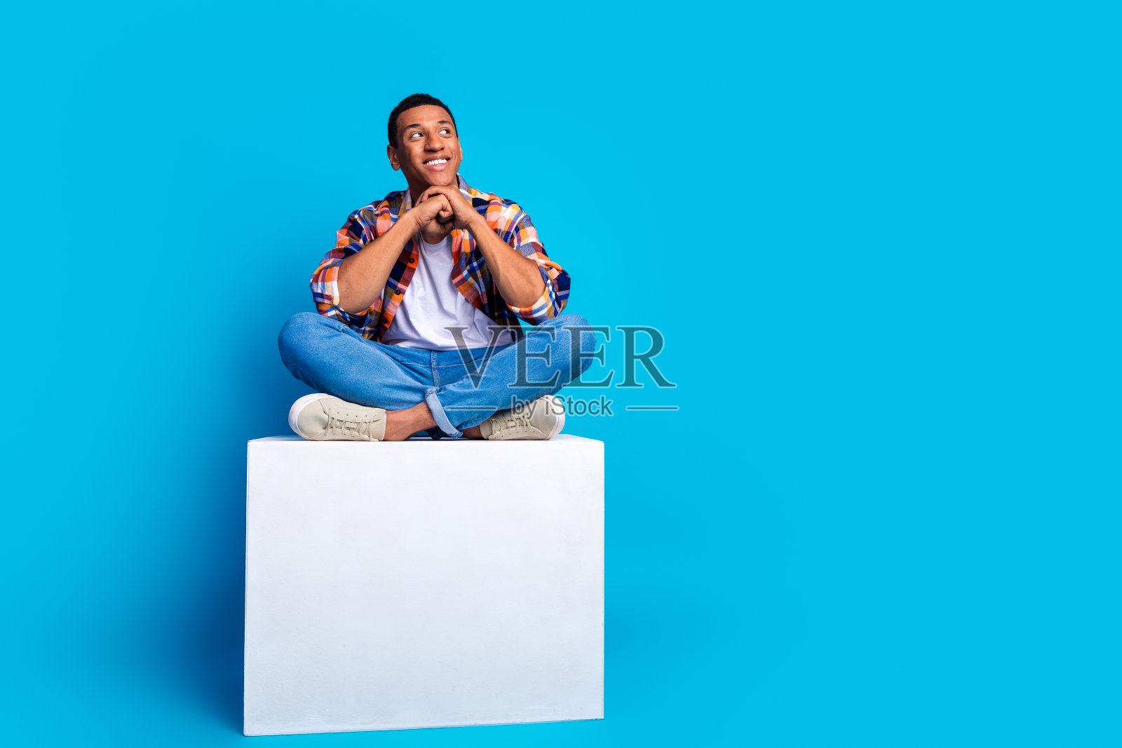 漂亮的年轻人的全尺寸照片，坐在讲台上，看起来空旷的空间，穿着衬衫孤立的蓝色背景照片摄影图片