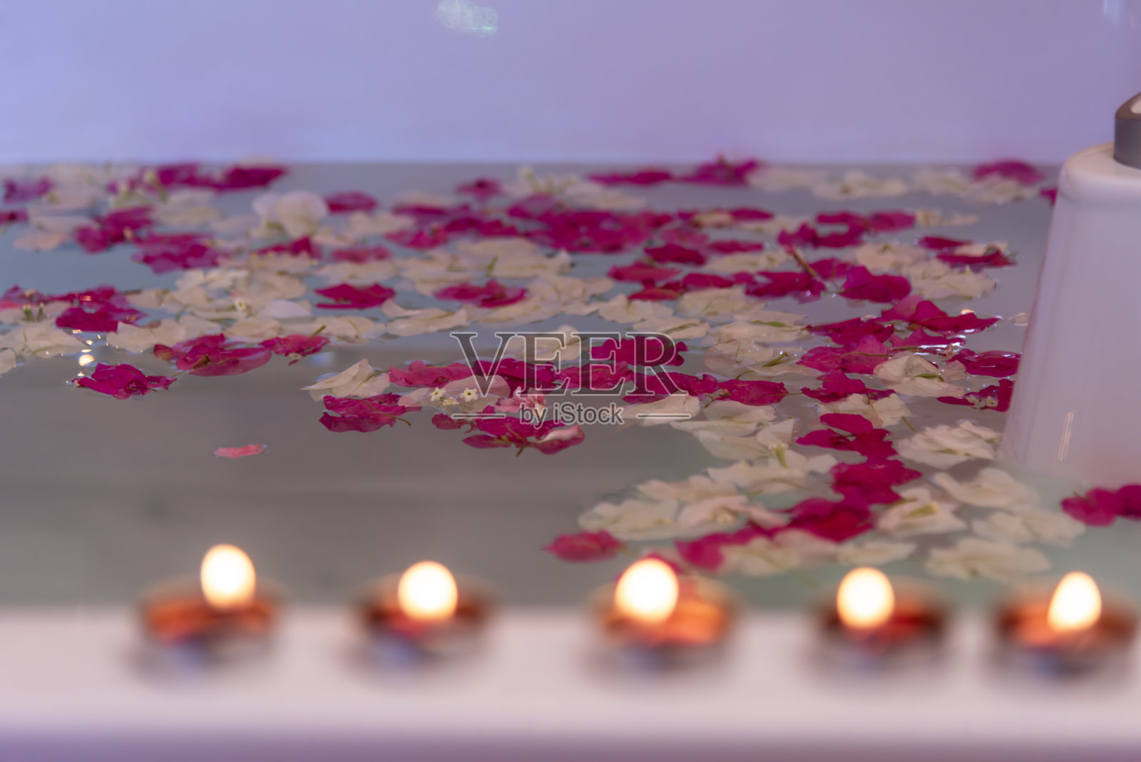 水疗帽浴缸与漂浮的玫瑰花瓣和红烛照片摄影图片