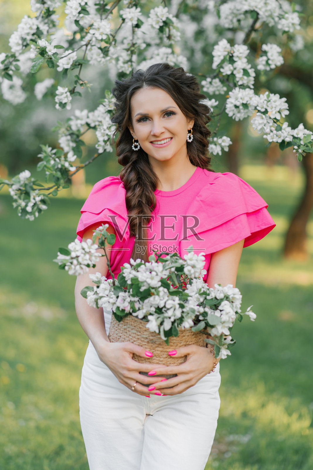 春天里，公园里，一个梳着辫子的年轻漂亮的欧洲女人，手里捧着一篮鲜花，站在盛开的苹果园里照片摄影图片