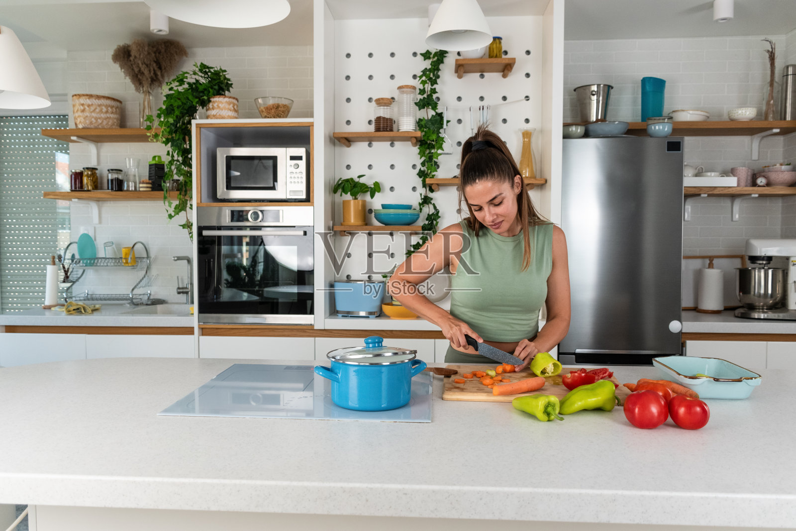 年轻的运动女性在月经期间准备健康餐。女性在月经期间在家庭厨房烹饪蔬菜。健康饮食搭配有机食品，午餐后在家锻炼照片摄影图片
