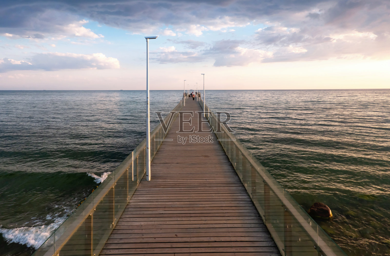 一个长长的海上码头的远景。有一条木板路和玻璃栏杆。早上的海景。远处可以看到人影。背景。照片摄影图片