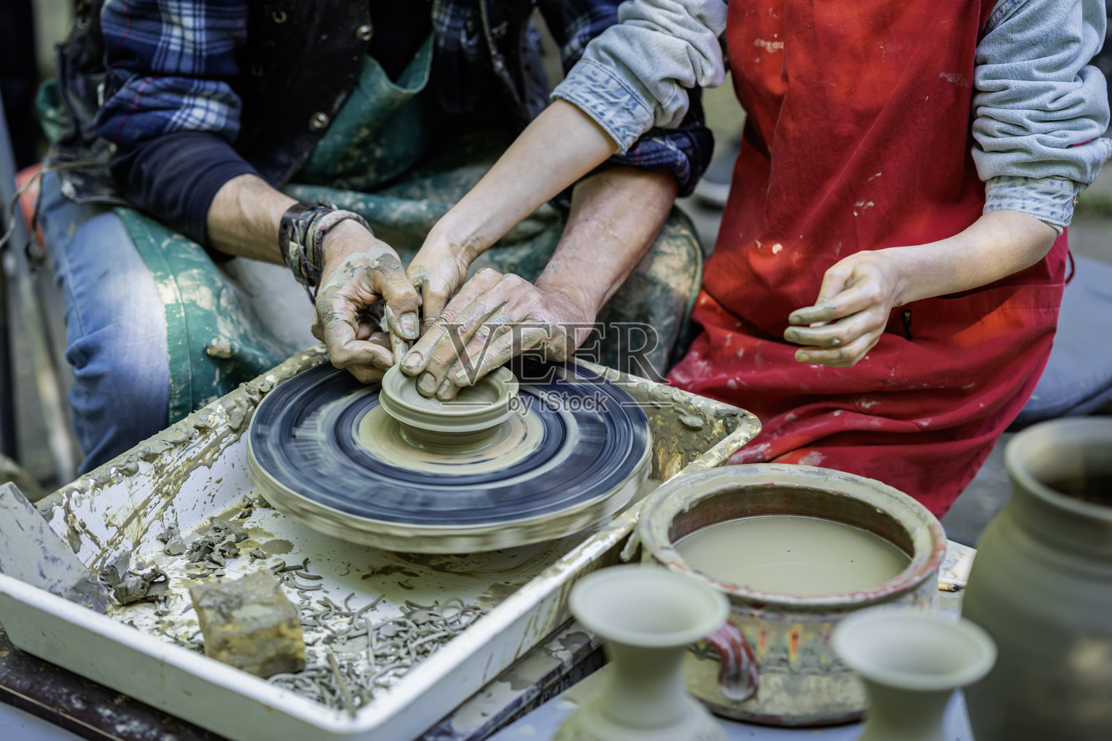 陶艺师教孩子在陶轮上制作陶罐，特写镜头照片摄影图片
