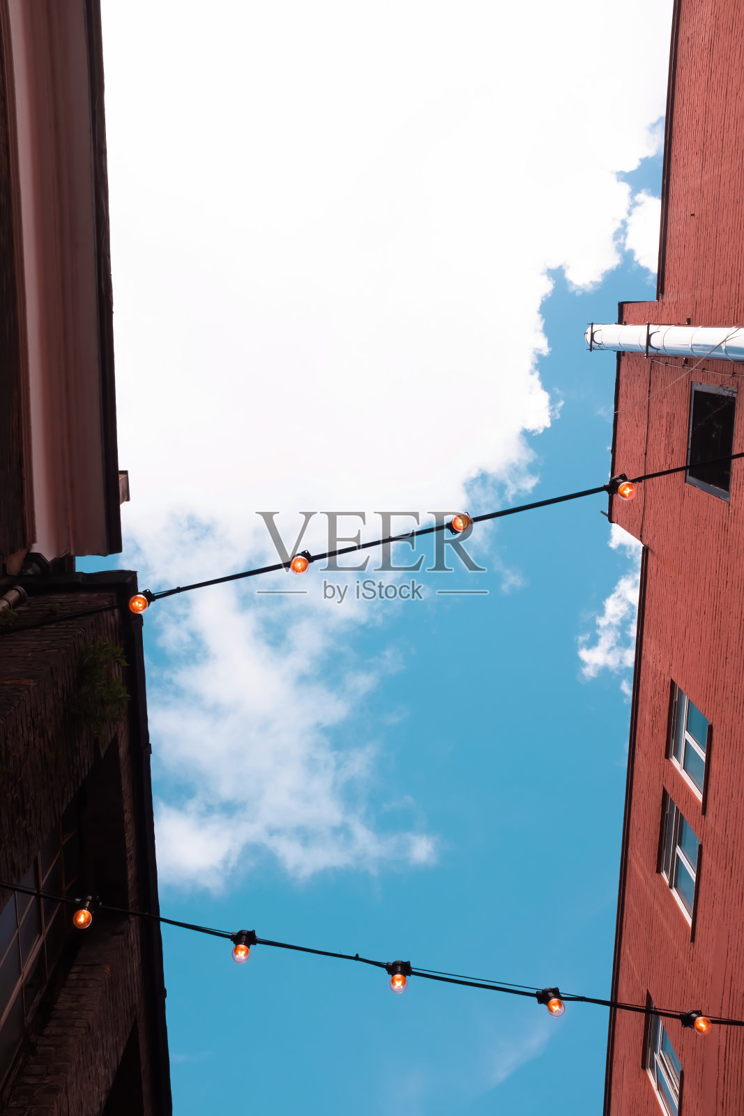 在伦敦市中心一条狭窄的小巷里，灯泡电线连接着两座砖砌建筑。照片摄影图片