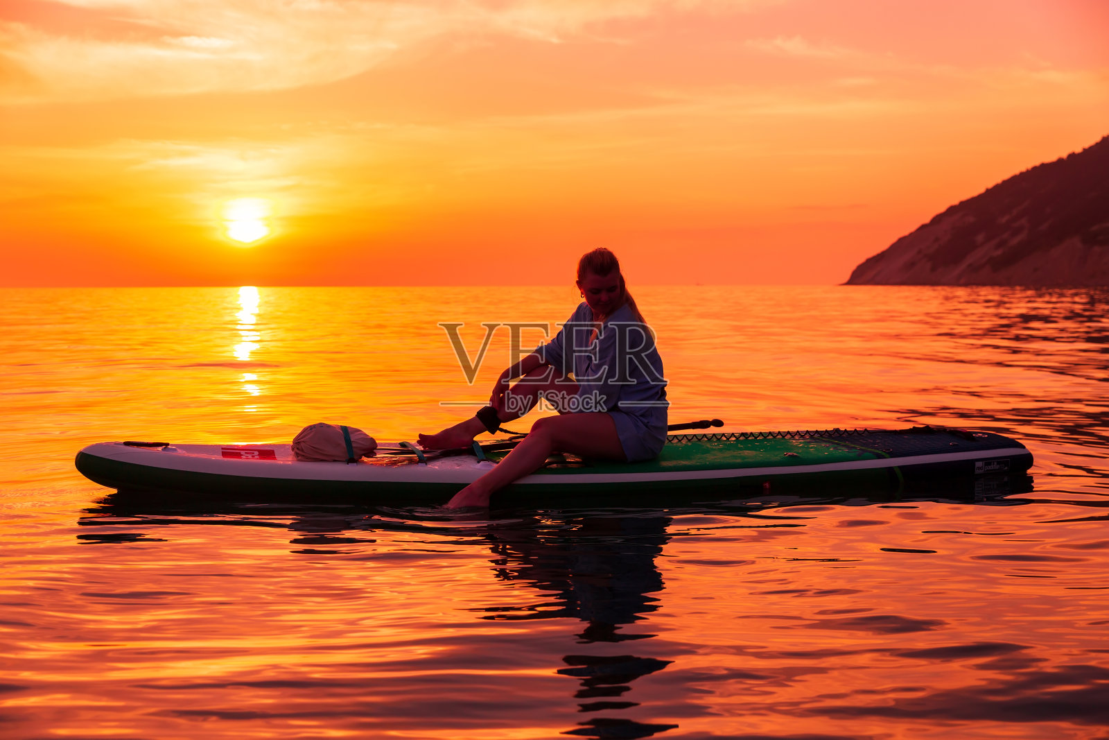 女人的剪影站立桨板在海上与日落或日出的颜色。红色桨板上的女人照片摄影图片