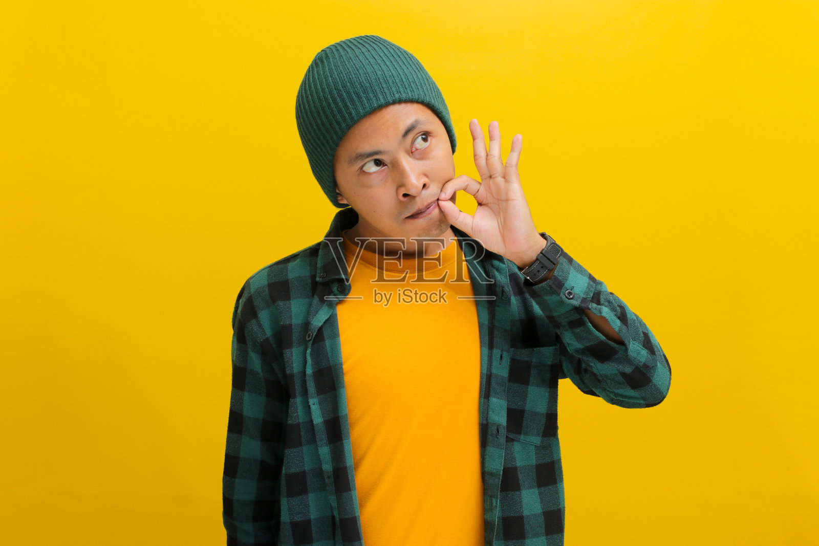 一名年轻的亚洲男子正在做一个沉默的手势，闭上他的嘴唇或拉上他的嘴照片摄影图片