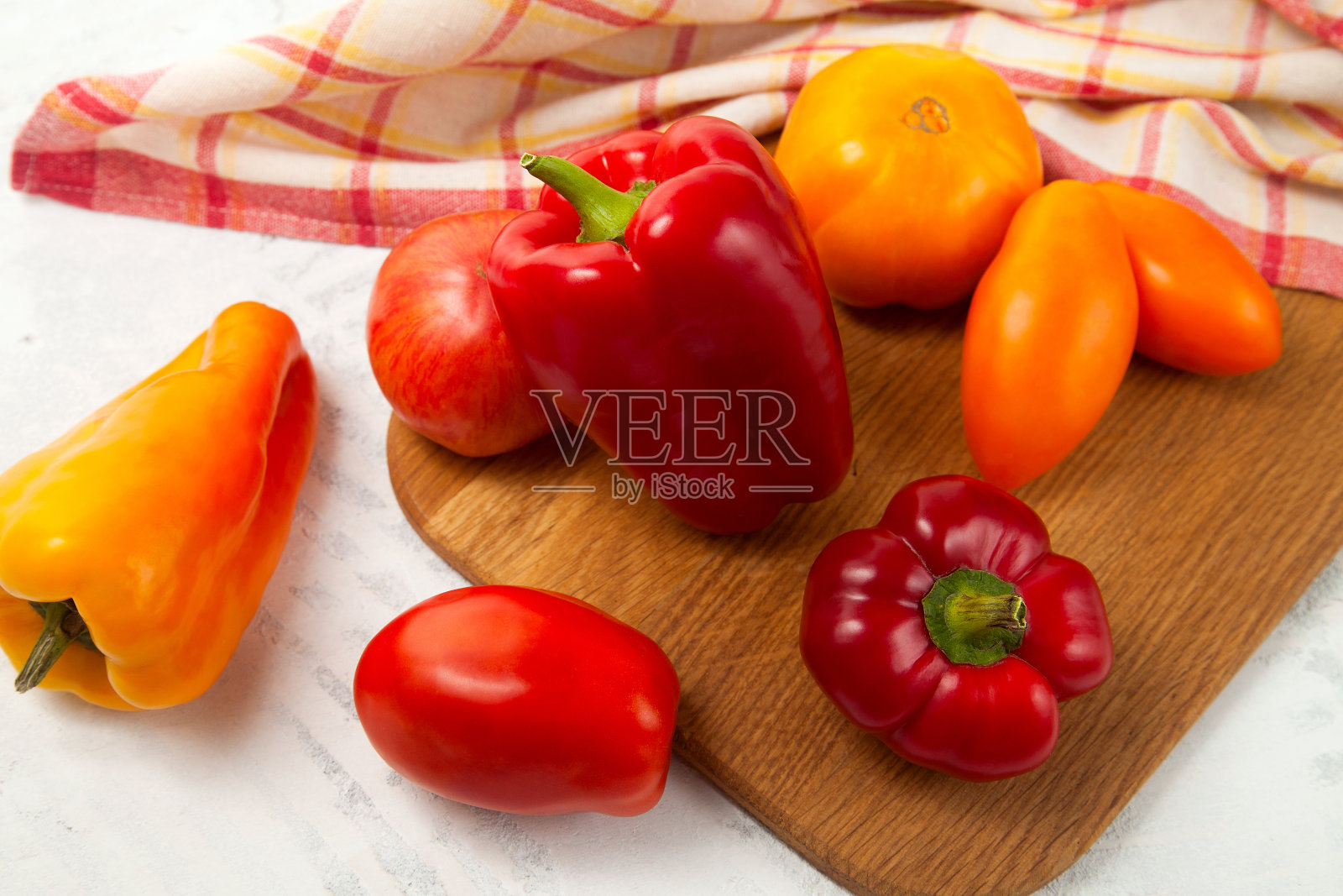 砧板上有几个红色和黄色的西红柿和甜椒在白色的木制背景和红色的厨房毛巾。照片摄影图片