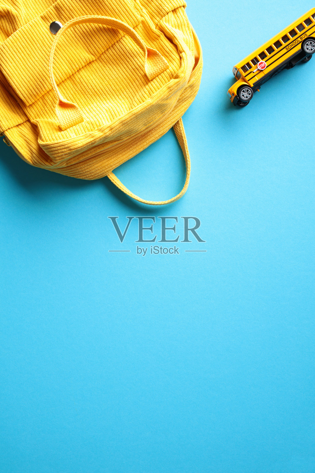 蓝色垂直背景上的黄色背包和校车。回到学校的概念。平躺，俯视图。照片摄影图片