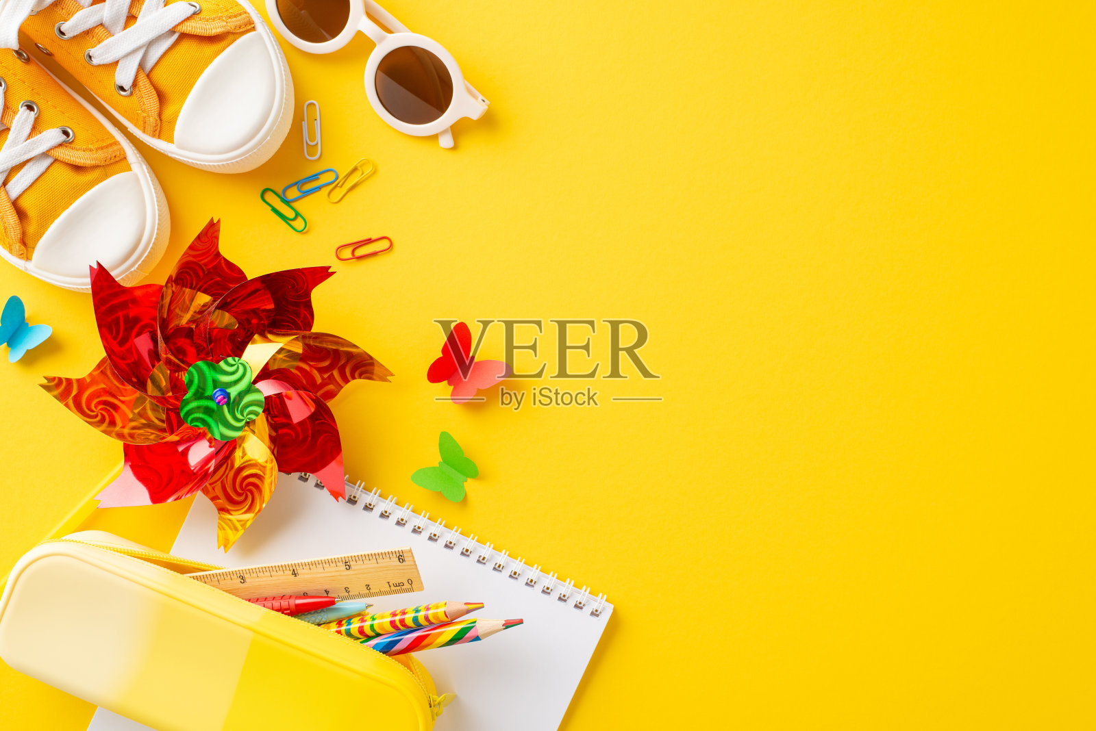 明亮而有趣的平面布置着孩子们的暑期学习用品，包括一个风车、运动鞋和一个笔记本，背景是充满活力的黄色照片摄影图片