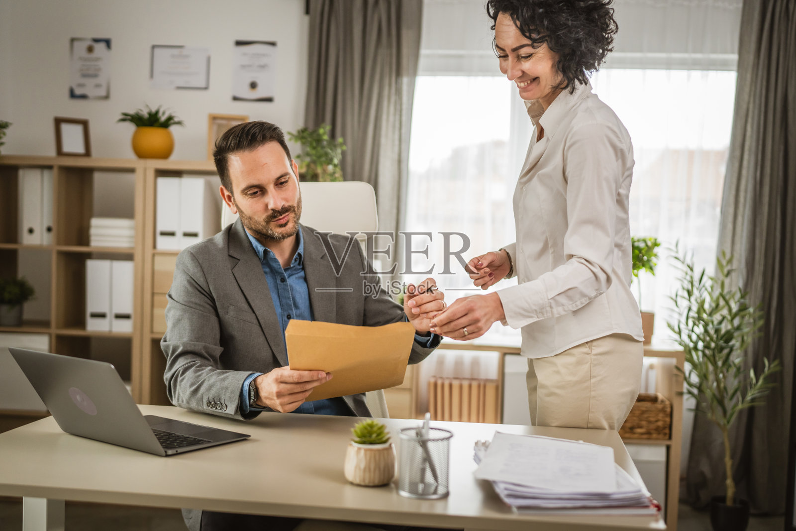 两个兴奋的同事在办公室打开装有文件的信封照片摄影图片