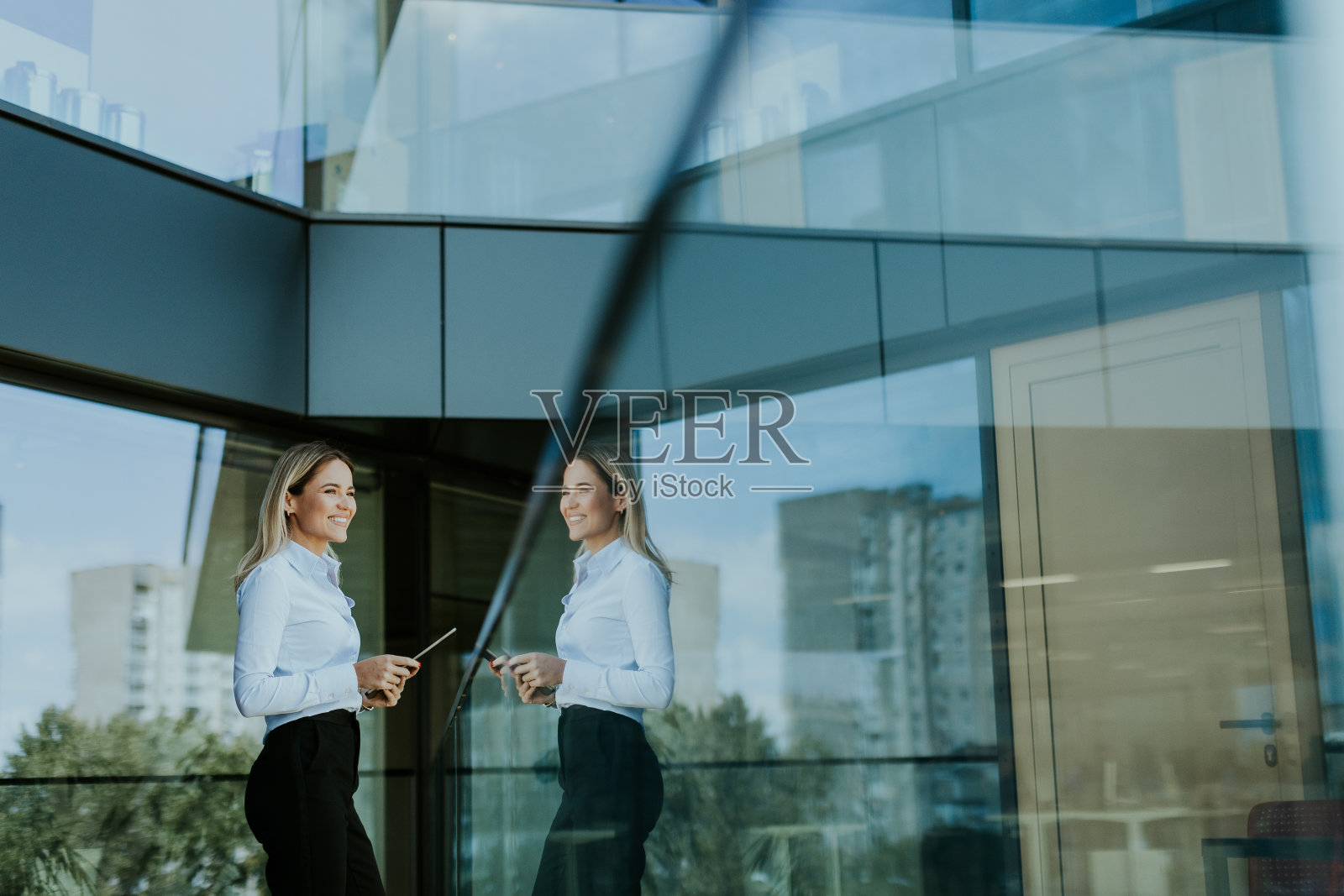 自信的女商人手持电子平板电脑，站在正午的现代办公楼外照片摄影图片