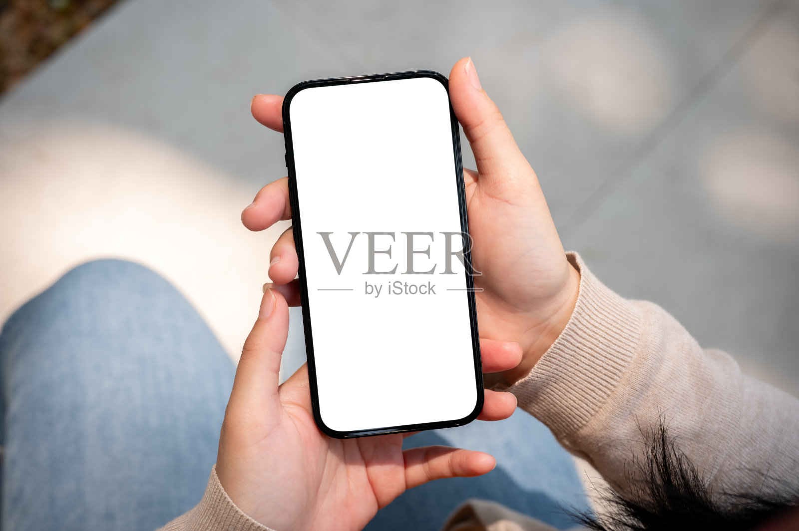 一个阳光明媚的日子里，一个穿着牛仔裤的女人坐在户外使用她的智能手机。照片摄影图片