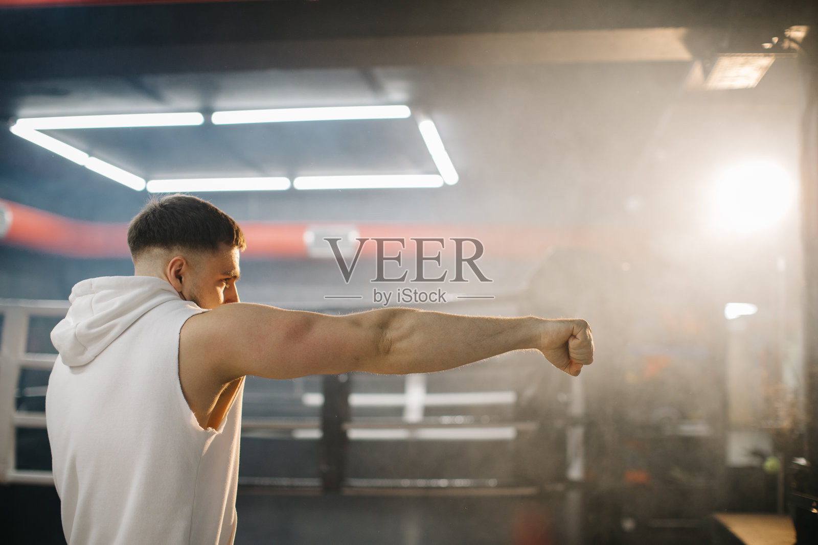 一个男拳击手正在拳击，拳击台的背景上有一个阴影。拳击手在拳击工作室练习出拳。照片摄影图片