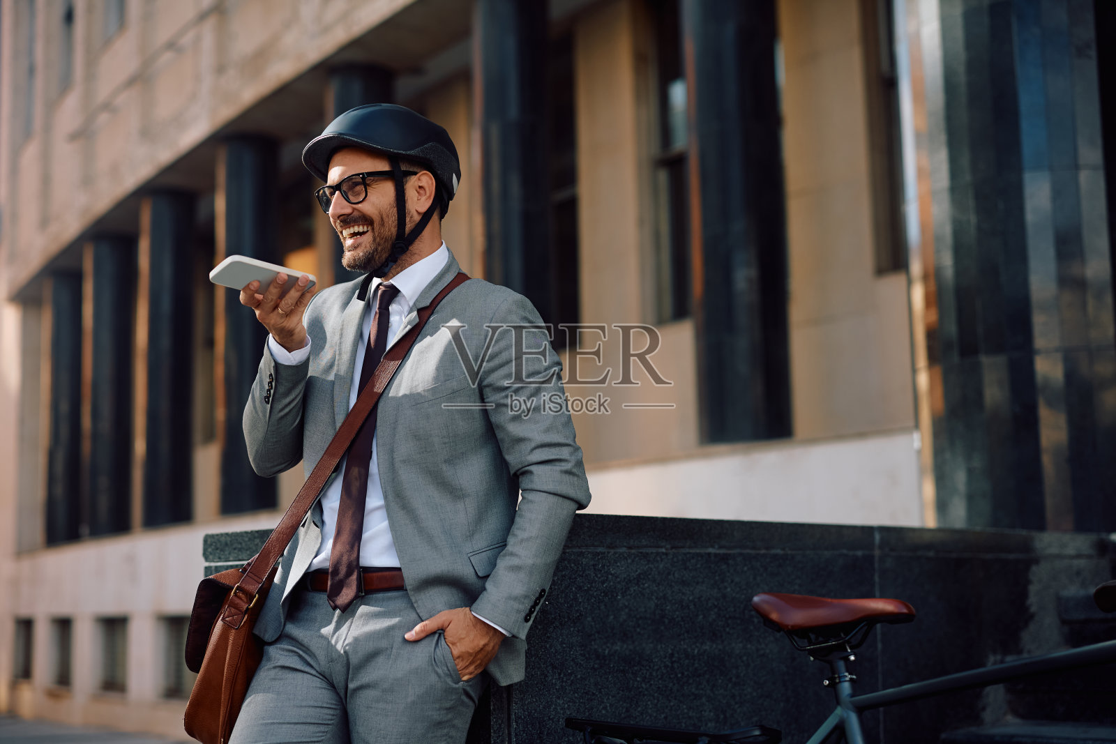 快乐的商人骑着自行车在城市街道上用手机交流。照片摄影图片