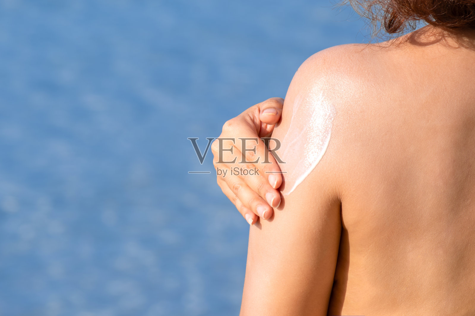 一位女士正在涂抹防晒霜和护肤品，以保护皮肤免受紫外线的伤害。她正在给她的手和胳膊涂防晒霜。太阳的标志是一个非常阳光的背景。健康护肤理念照片摄影图片