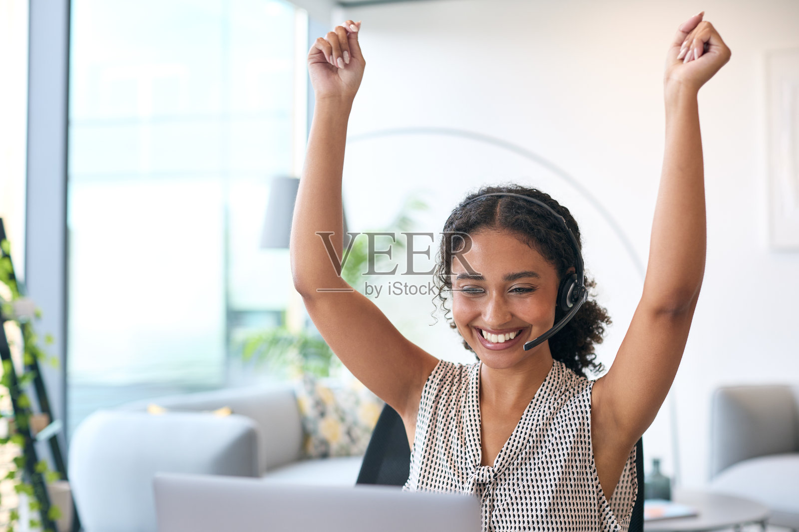 戴耳机的女人坐在办公桌前用笔记本电脑庆祝好消息或达到销售目标照片摄影图片