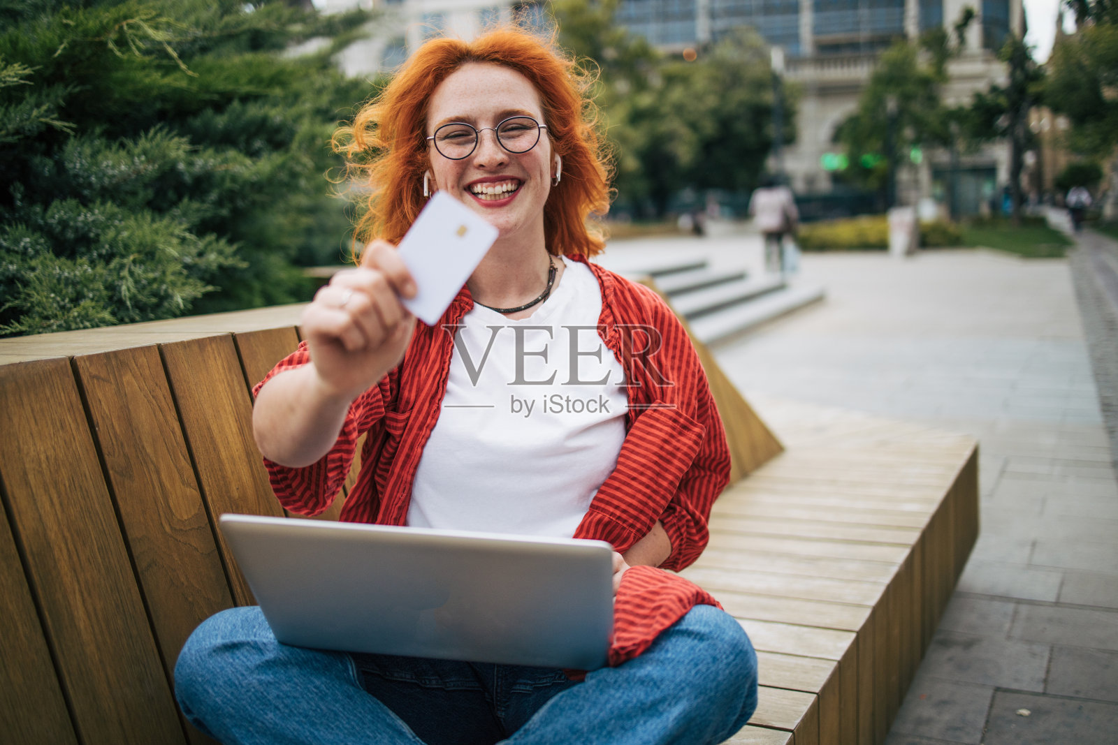 微笑的年轻女子拿着信用卡，用着笔记本电脑。照片摄影图片