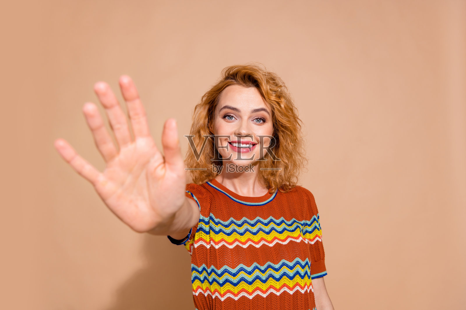 友好积极的女孩的肖像，姜黄色的发型，穿着针织t恤给你击掌说你好，孤立的米色背景照片摄影图片