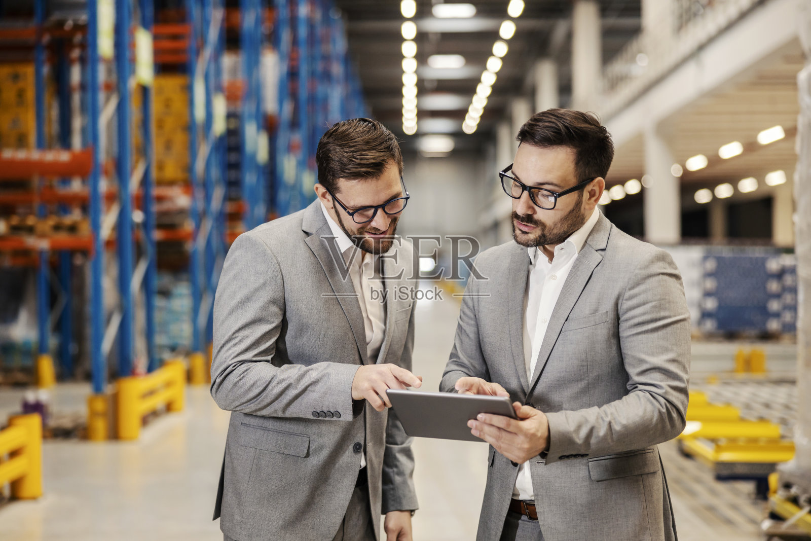 商人们在仓库里散步时看着平板电脑。照片摄影图片