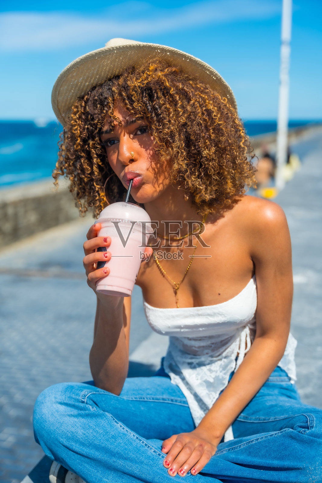 性感的女人坐在海边吮吸奶昔照片摄影图片