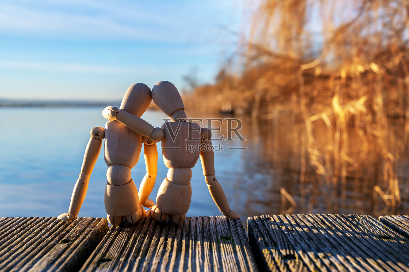 两个木头人依偎在湖岸的木堤上，象征着爱情和伙伴关系照片摄影图片