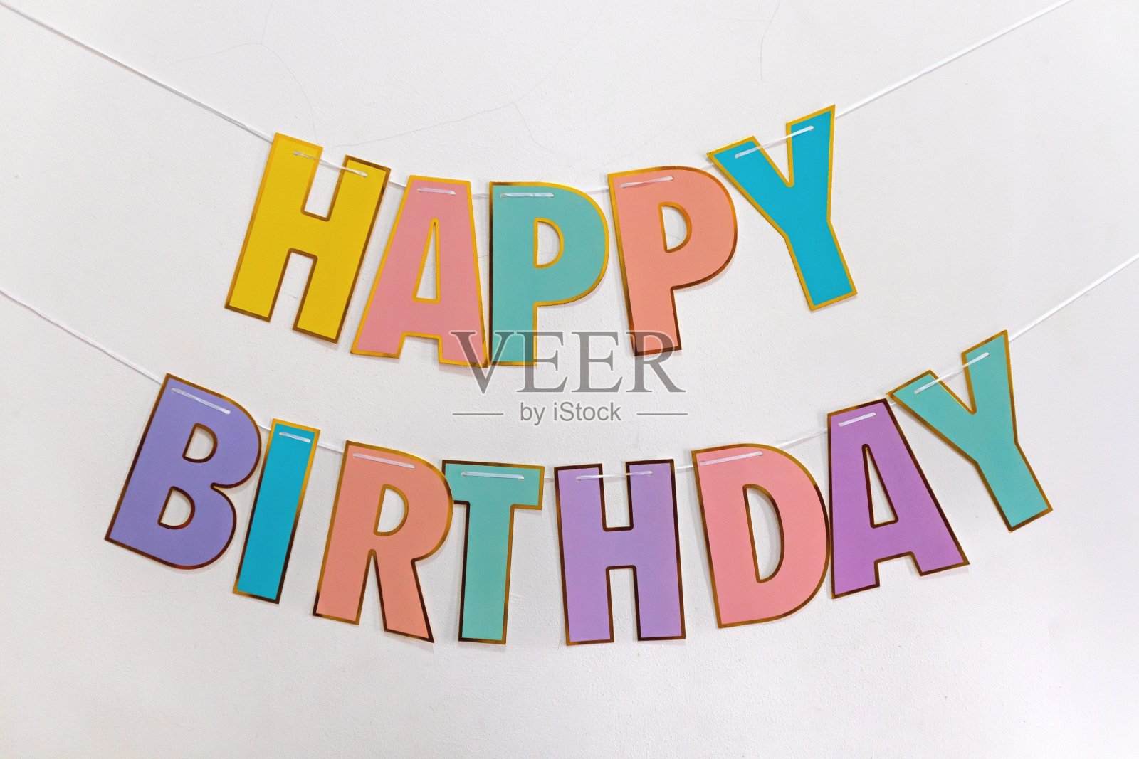 白色墙上的彩色横幅上写着“生日快乐”。生日短信快乐。照片摄影图片