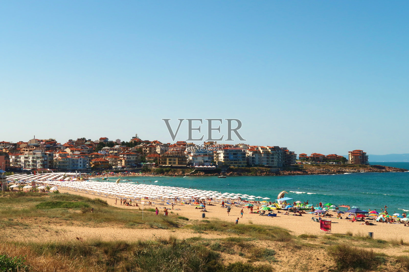 在繁忙的一天里，可以看到许多白色的沙滩伞和沙滩上的太阳椅，强烈的蓝绿色大海和索索波尔镇，背景是保加利亚的索索波尔照片摄影图片