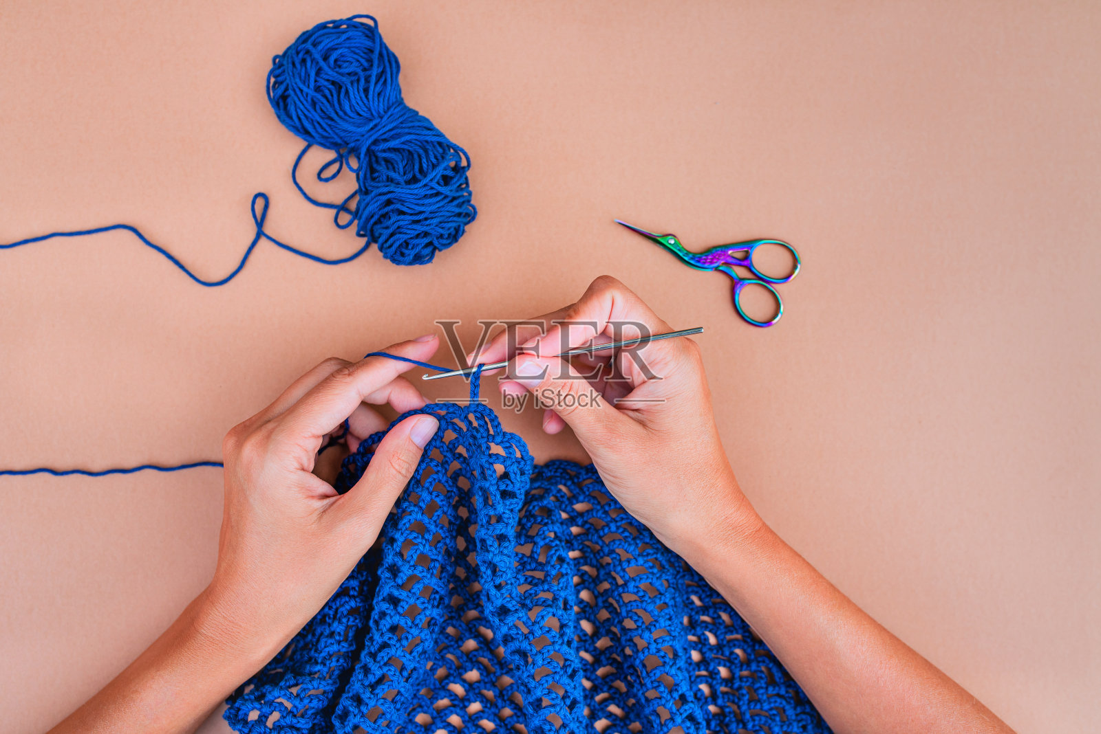 在米色背景上编织蓝色网的手的观点。照片摄影图片