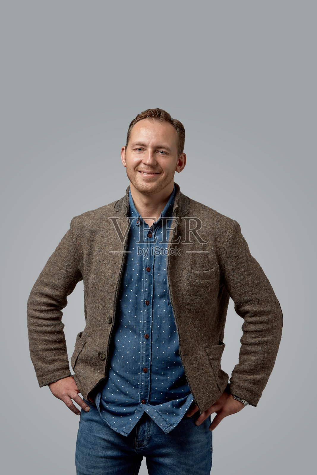 穿着皮夹克、双手插在口袋里、面带微笑的休闲老人站在工作室灰色的墙上照片摄影图片