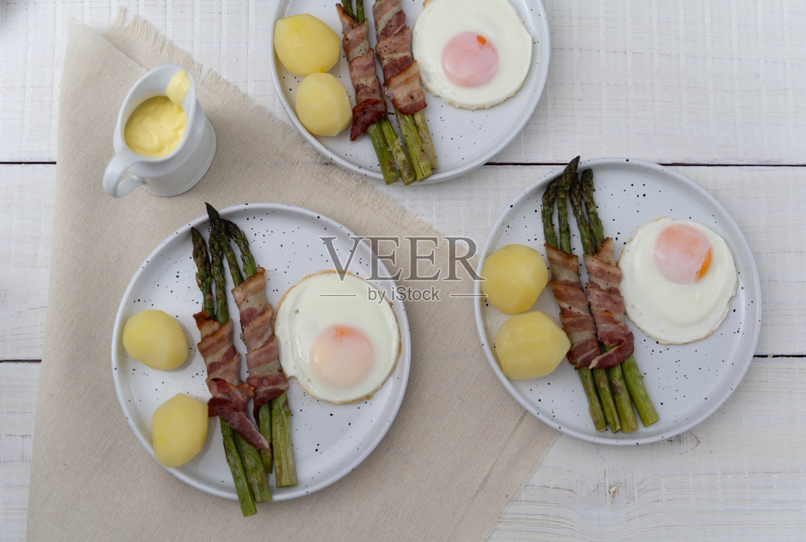 用培根裹着烤好的绿芦笋，配上煮熟的土豆和鸡蛋，放在漂亮的白色盘子里，木质的表面很轻照片摄影图片