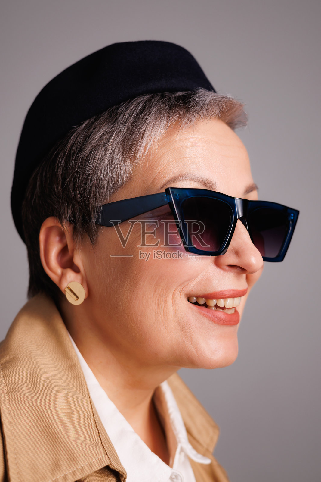肖像中微笑的成熟女性戴着时尚的太阳镜，戴着贝雷帽，穿着灰色裁剪的风衣照片摄影图片
