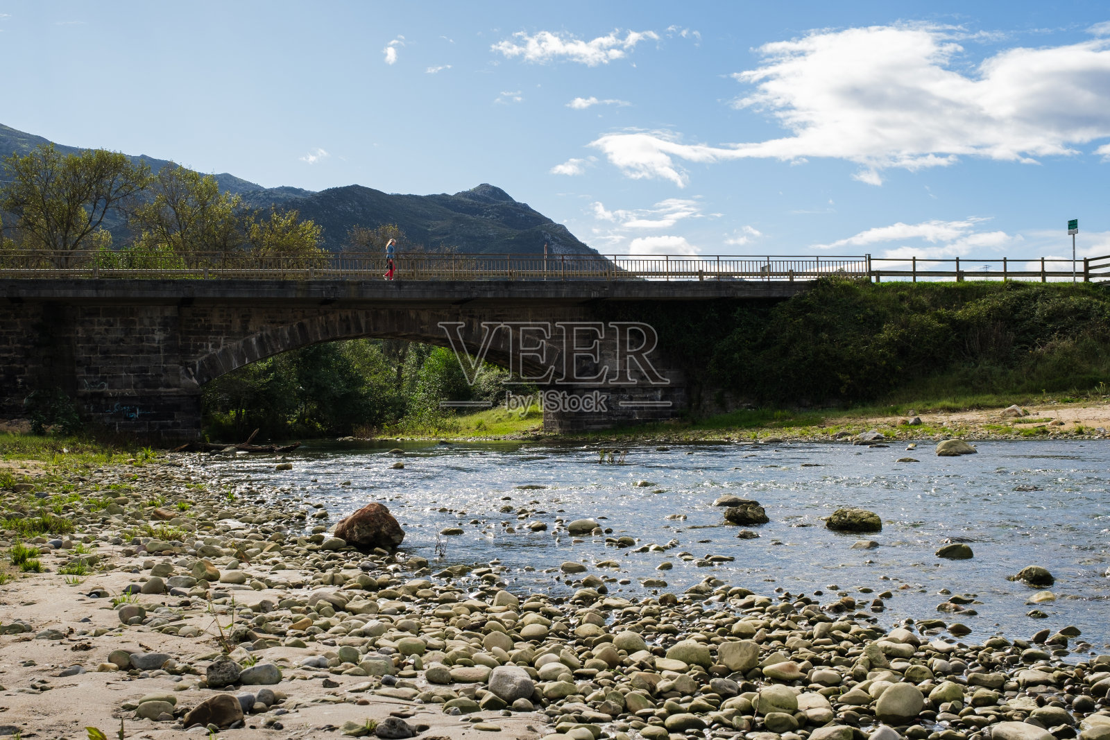 一个穿着红色长袜的女孩穿过小溪上的一座桥。照片摄影图片