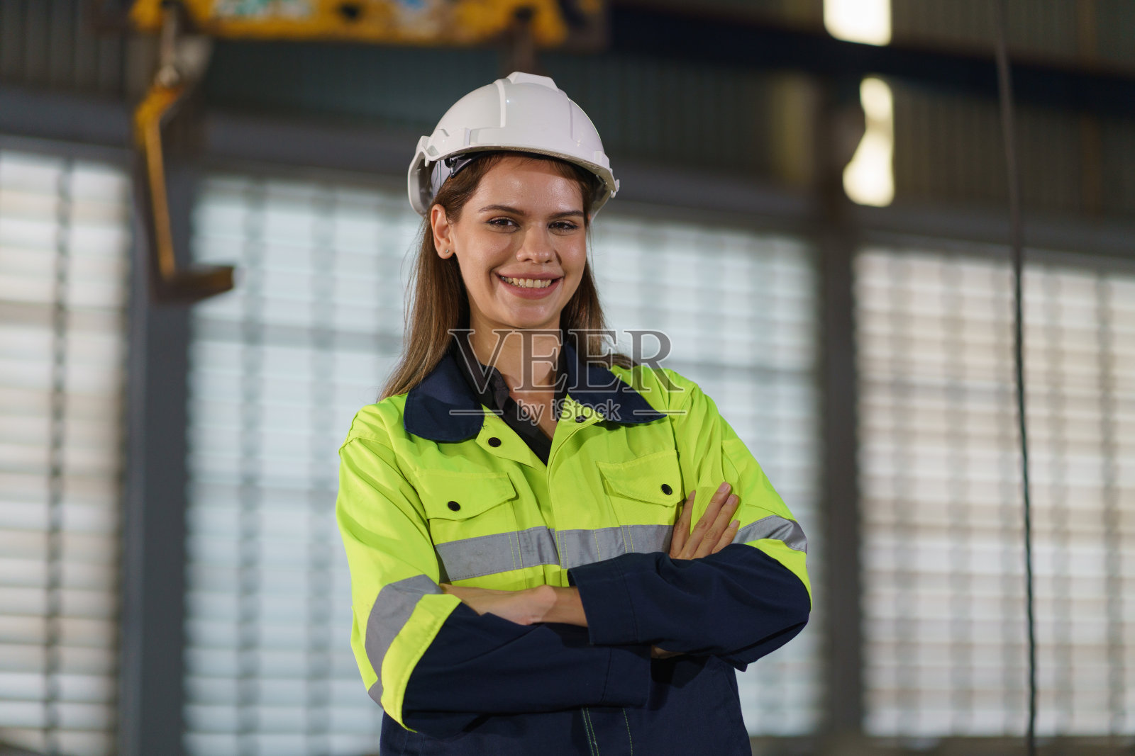 身穿绿色制服、头戴安全头盔的女工在一家金属板材厂内进行质量检查。照片摄影图片