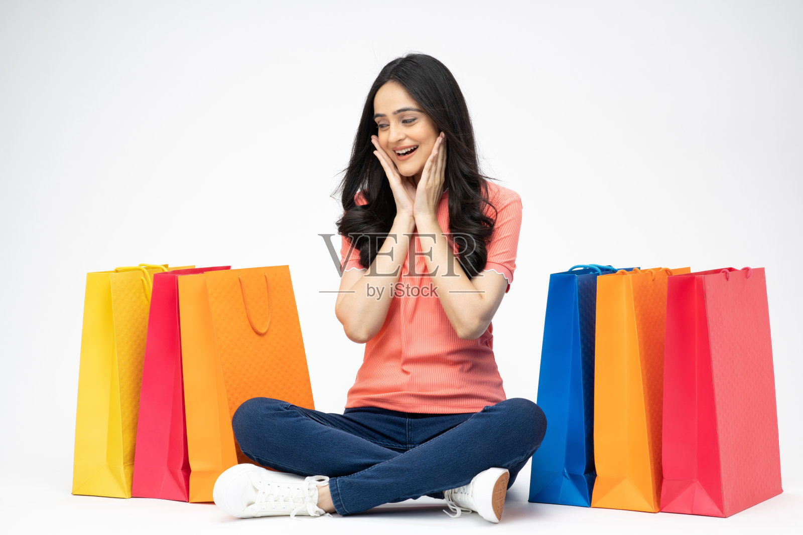 年轻女孩的全身肖像坐在拿着购物袋开朗孤立的白色背景股票照片照片摄影图片