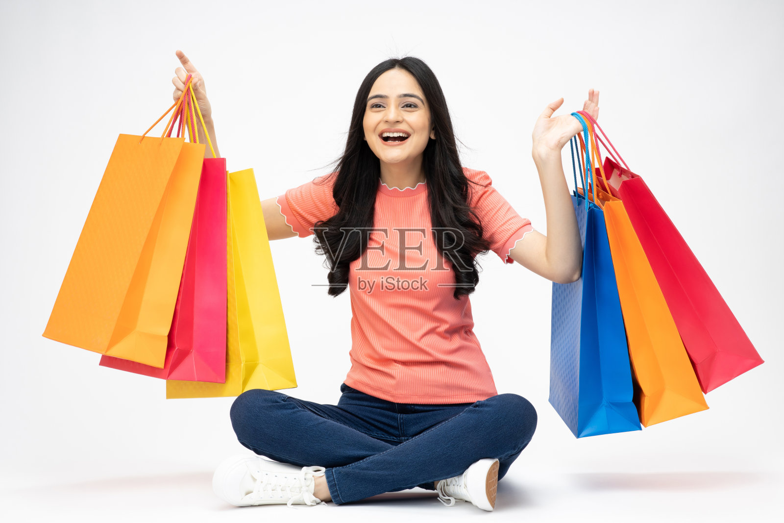 年轻女孩的全身肖像坐在拿着购物袋开朗孤立的白色背景股票照片照片摄影图片