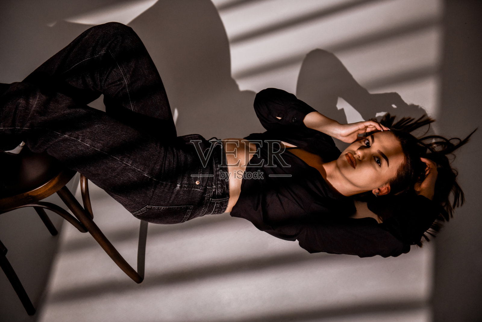 可爱的女性在阴影中躺在地上，把脚放在椅子上照片摄影图片