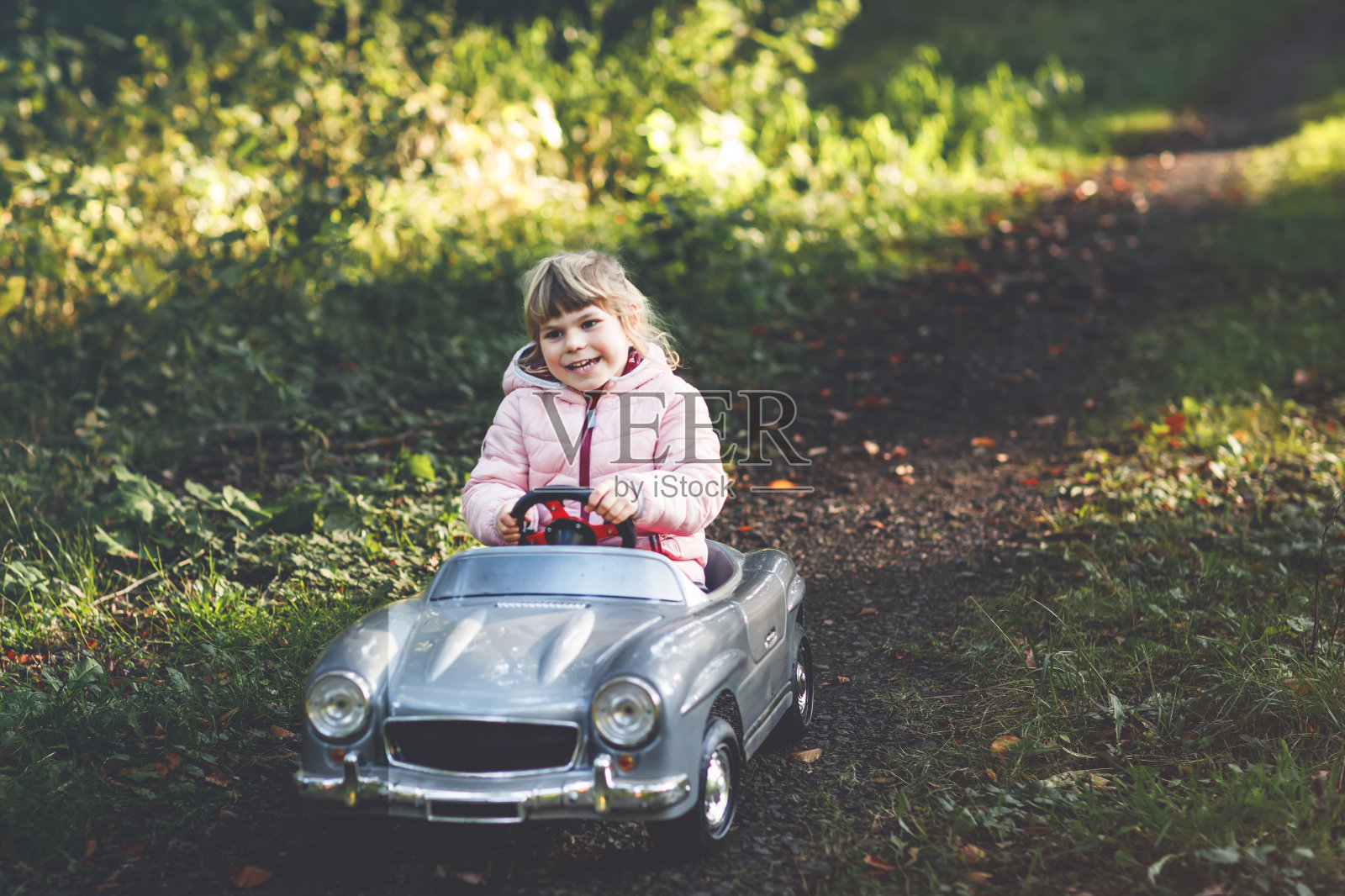 学前班的小女孩开着老式玩具车。快乐的孩子在户外玩耍。活跃的学龄前儿童在森林里享受温暖的秋日。笑容灿烂的孩子在玩耍照片摄影图片