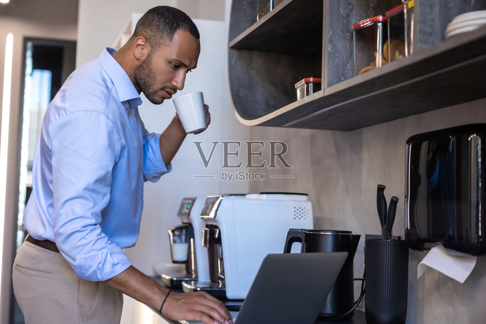 穿着蓝色衬衫的非裔美国人在厨房用笔记本电脑工作照片摄影图片