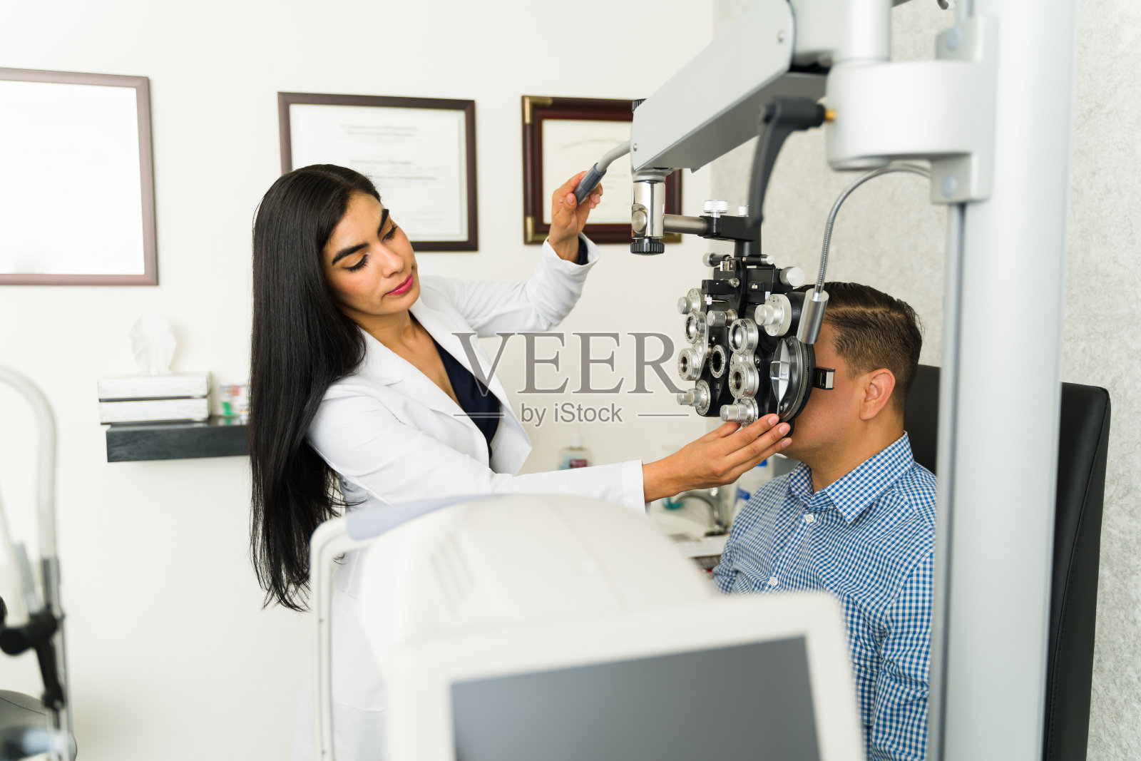在诊所的检查室里，一位专业的女眼科医生一边调整设备，一边检查一位男病人的视力照片摄影图片