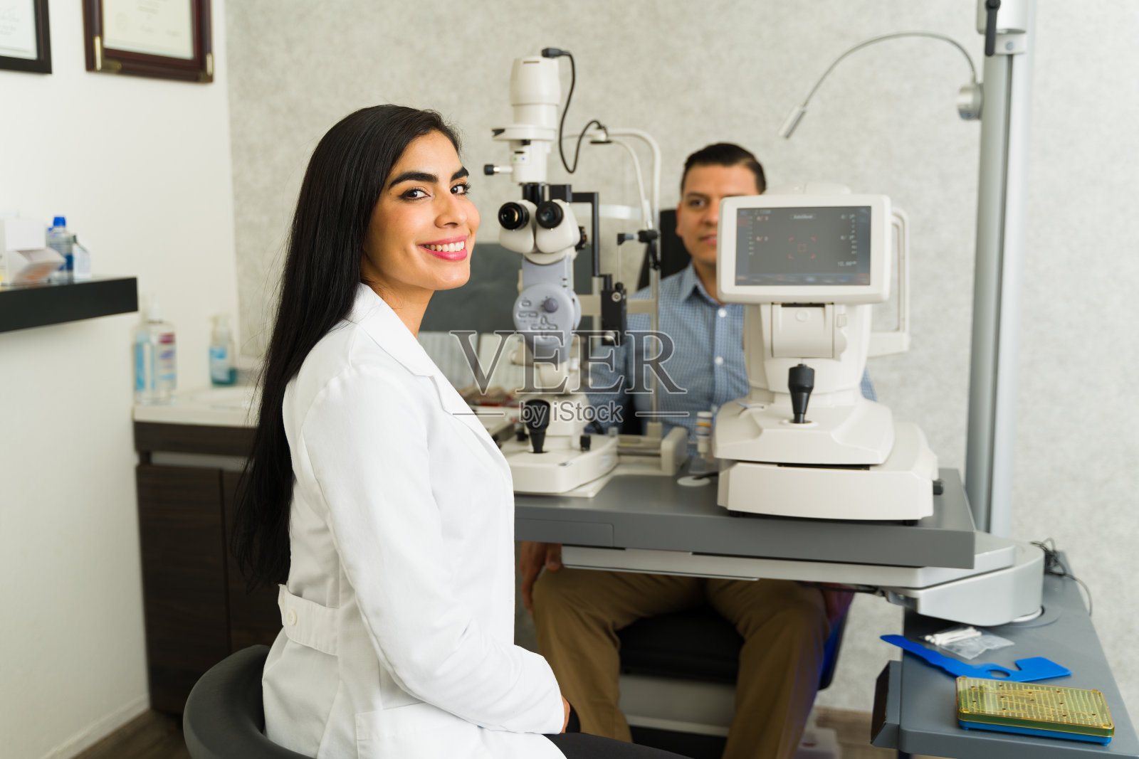 一位自信的女验光师面带微笑，在一家现代眼科医生的办公室里为一位男病人做视力检查照片摄影图片