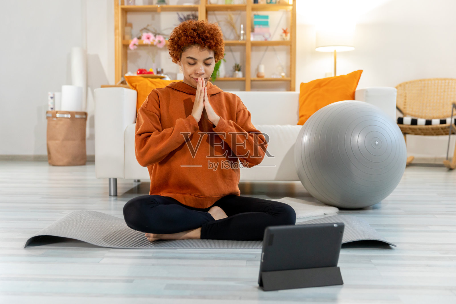 瑜伽正念冥想。年轻健康的非洲女孩在家练习瑜伽。女子在瑜伽垫上以莲花姿势坐着，眼睛闭着双手在室内祈祷冥想。女孩在做呼吸练习。照片摄影图片