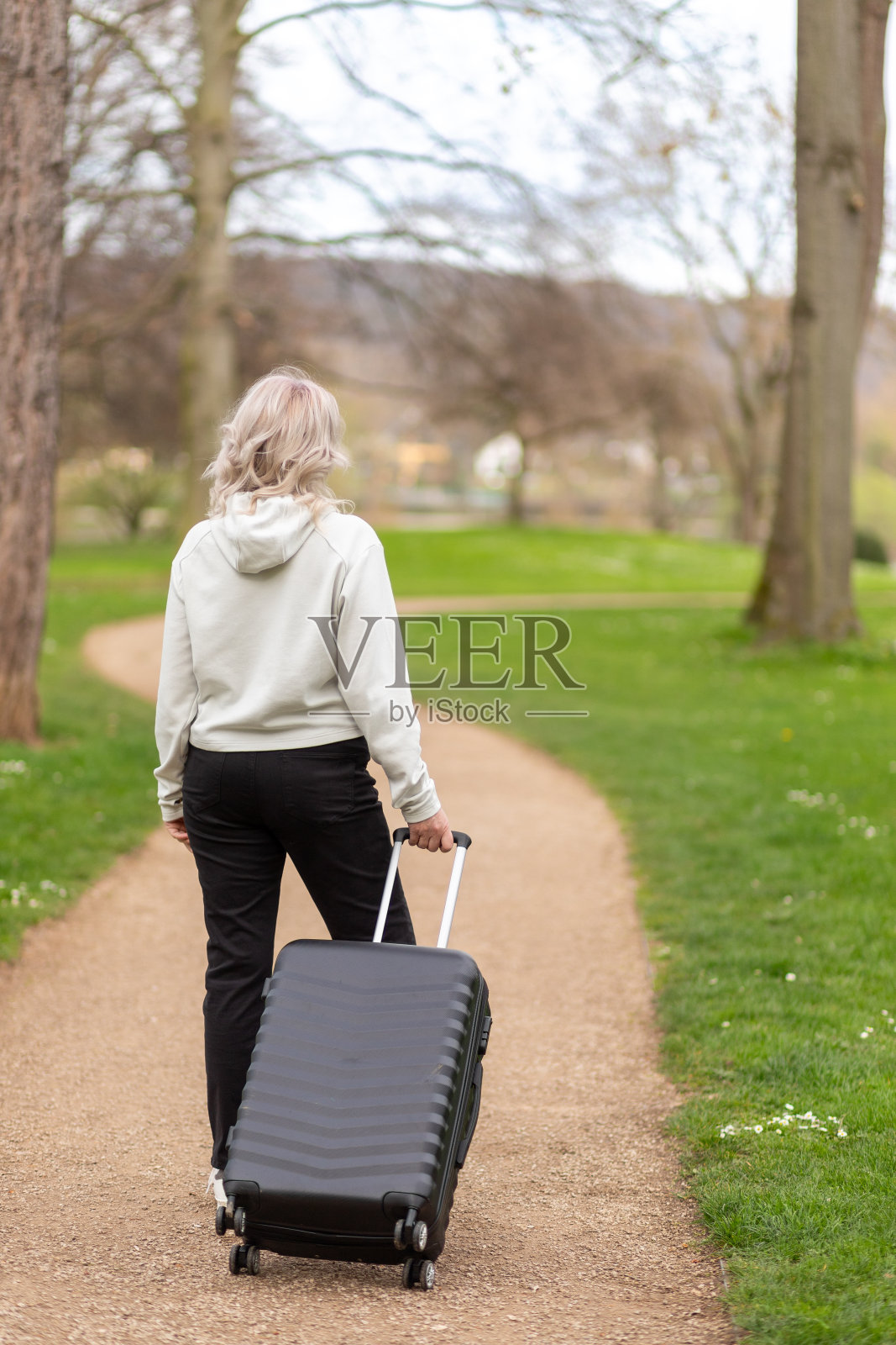 一名女子拎着行李箱走在公园小路上，背对着镜头照片摄影图片